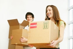 A young couple carries boxes for donation in front of a plain white background