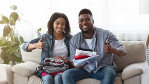 A picture of a smiling Black couple, holding clothes for donation in their laps as they each give a thumbs-up