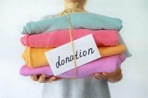 A person holds out a pile of colorful folded clothing that is held by a string with a label that says "donation"