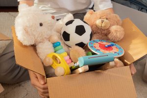A person is holding a cardboard box overflowing with toys