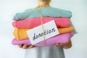 A person holding a stack of clothing wrapped in twine with a sign that says "donation" tucked in between the clothes and twine