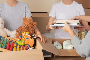 Three people working together to pack toys and books into cardboard boxes